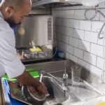 Chef washing pans at a stainless steel sink in a Dubai restaurant kitchen, where grease trap cleaning keeps drains flowing