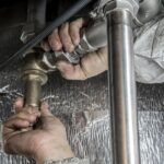 Plumber fitting stainless steel and brass pipework under a commercial kitchen unit during grease trap installation